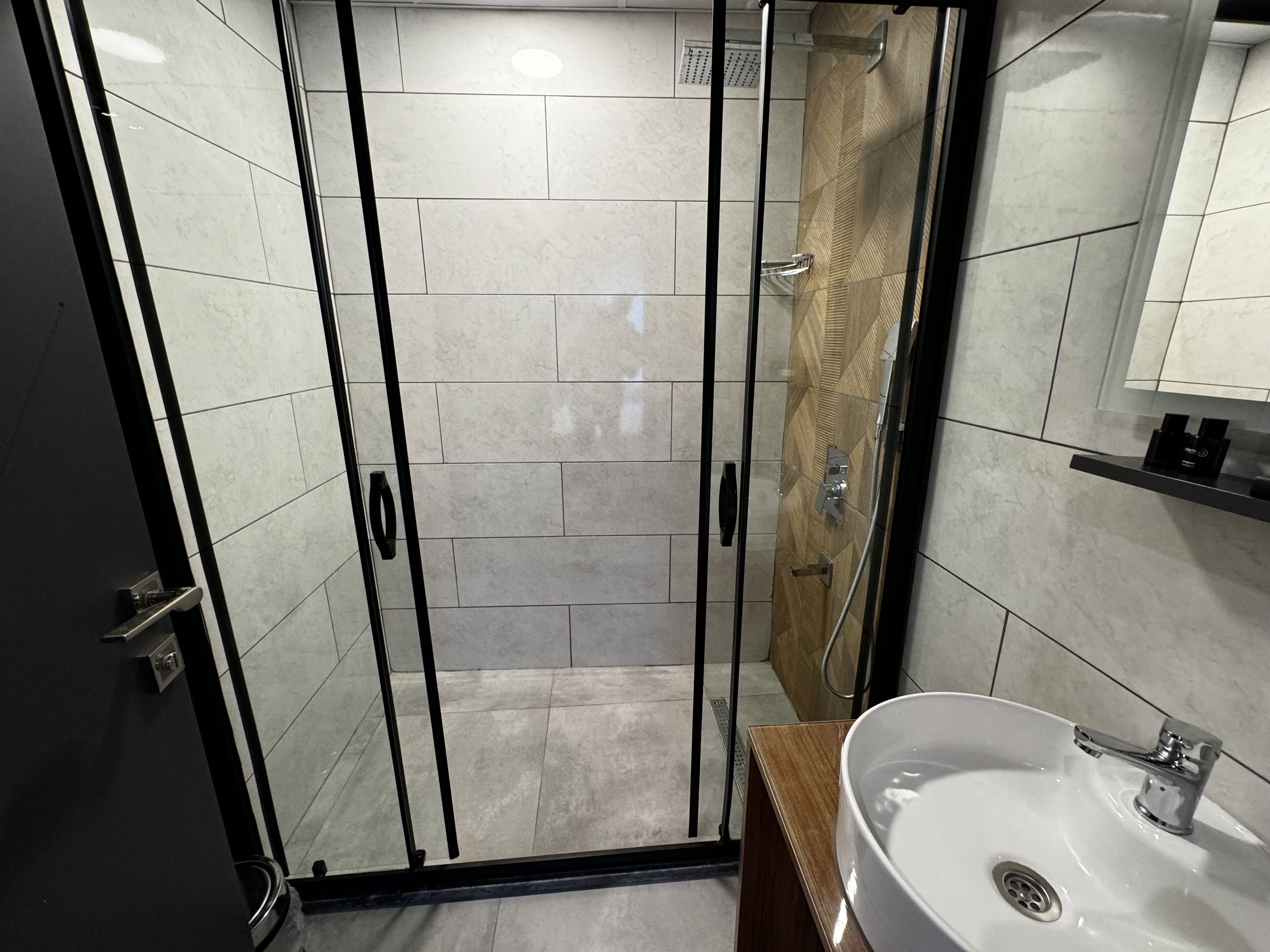 A modern bathroom with a glass-enclosed shower, a white sink, and a wooden vanity.