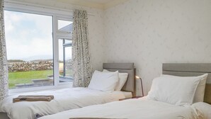A hotel room with two beds, a large window with a view of a grassy area, and a stone wall outside. - 3 bedroom accommodation in Southerness, near Sandyhills (Southerness, near Sandyhills)