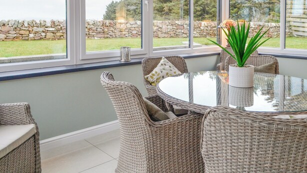 A conservatory with wicker furniture, a glass table, and a view of a stone wall and greenery. - 3 bedroom accommodation in Southerness, near Sandyhills (Southerness, near Sandyhills)