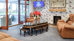 A living room with a sofa, a coffee table with a vase of flowers, a television, and a fireplace. - 3 bedroom accommodation in Southerness, near Sandyhills (Southerness, near Sandyhills)