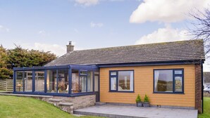 A two-story house with a conservatory, a stone chimney, and a paved front garden. - 3 bedroom accommodation in Southerness, near Sandyhills (Southerness, near Sandyhills)