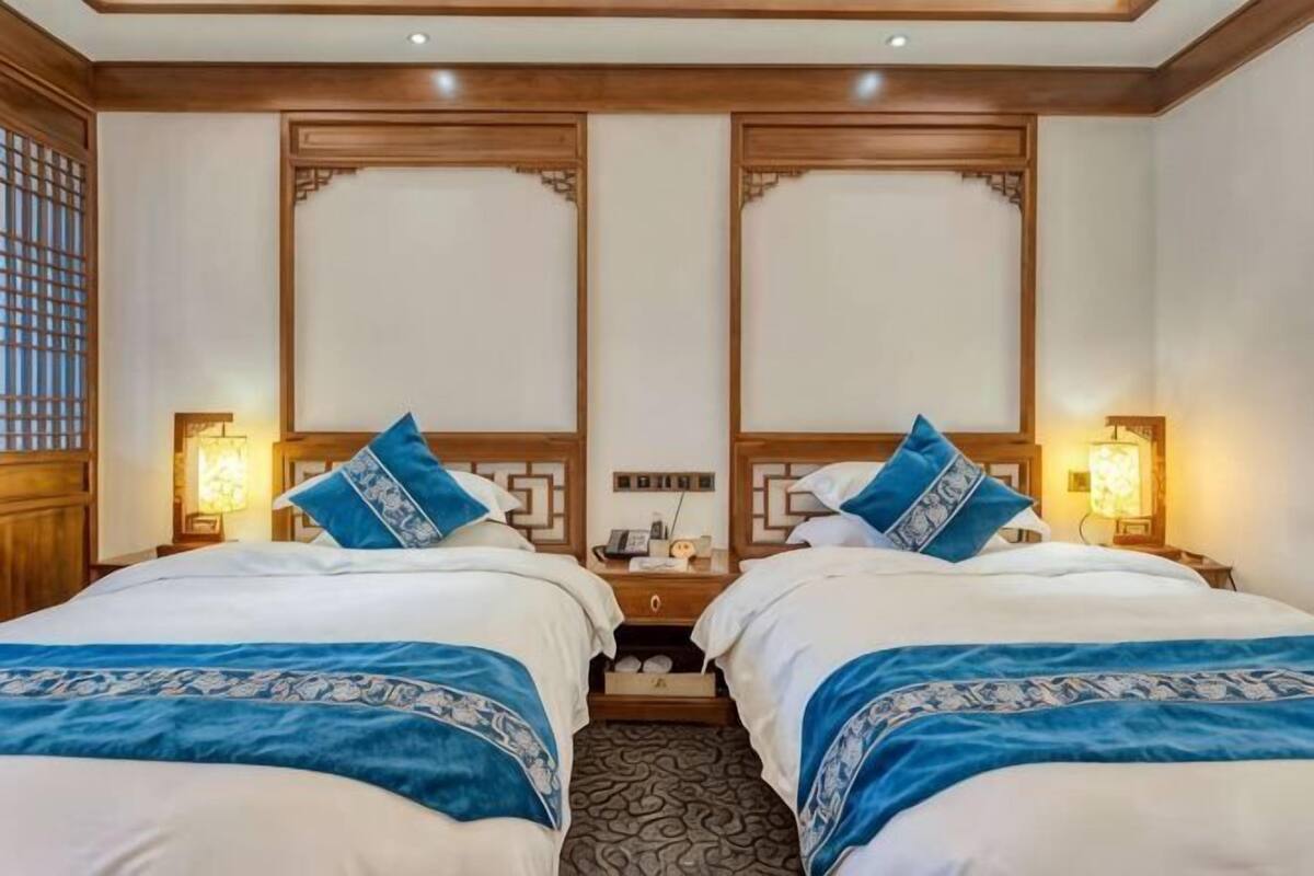 Une chambre d’hôtel avec deux lits, des têtes de lit en bois, des lampes de chevet et une moquette à motifs.
