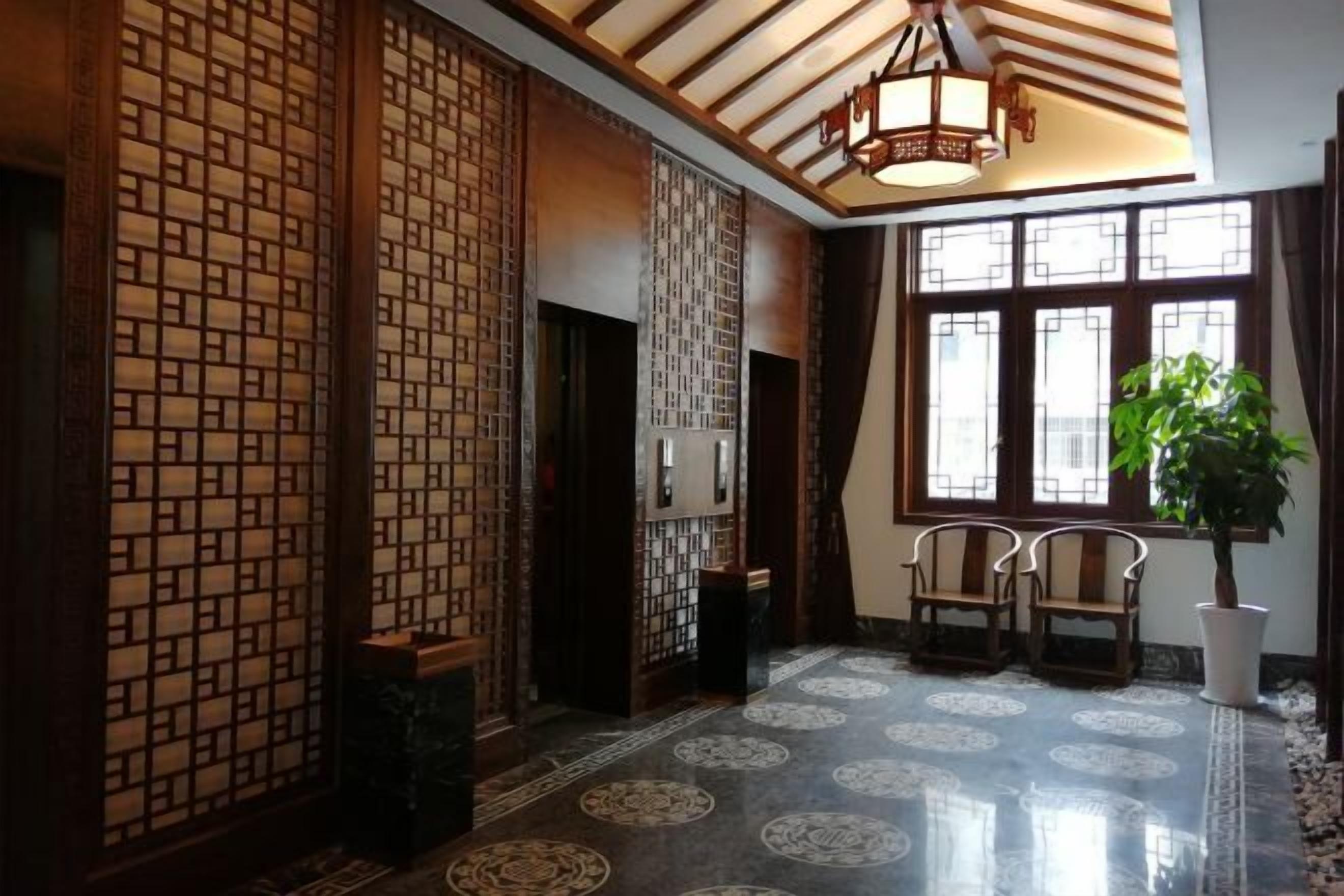 A traditional interior with wooden lattice partitions, a tiled floor with circular patterns, and a large window with a plant.
