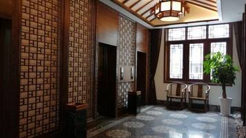 A traditional interior with wooden lattice partitions, a tiled floor with circular patterns, and a large window with a plant.