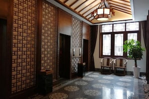 Un intérieur traditionnel avec des cloisons en treillis de bois, un sol carrelé orné de motifs circulaires et une grande fenêtre avec une plante.