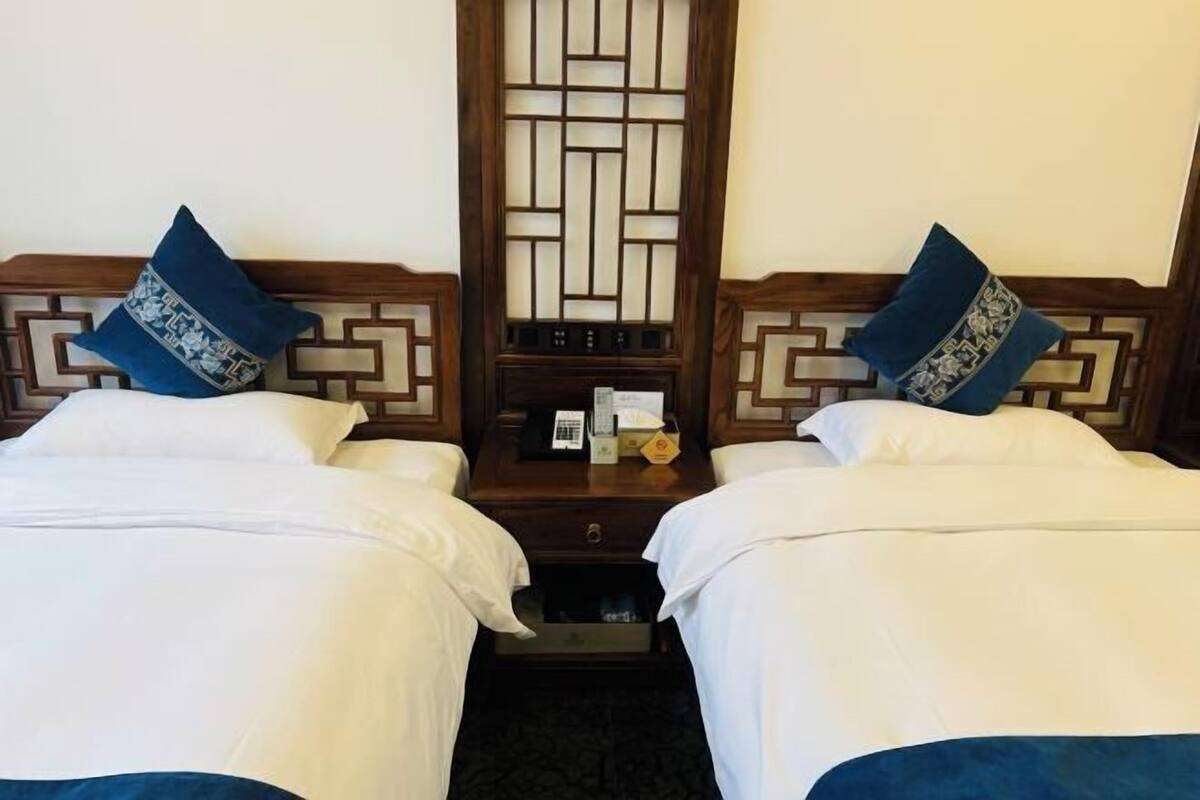 Une chambre d’hôtel avec deux lits, chacun étant équipé d’un oreiller et d’une table de chevet sur laquelle se trouvent un téléphone et une petite boîte.