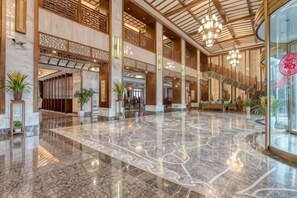 A spacious lobby with a marble floor, wooden columns, and a staircase leading to upper levels.