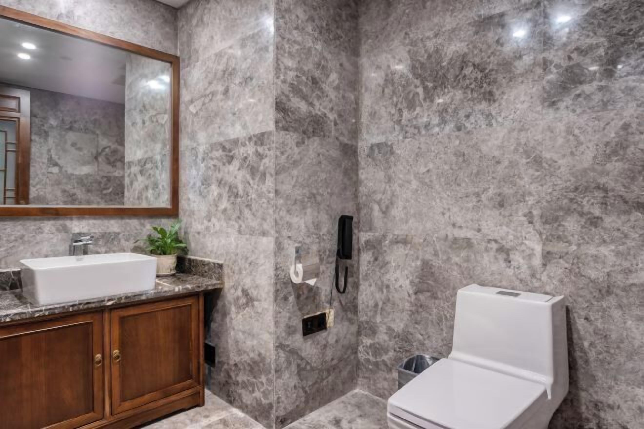 A bathroom with a marble wall, a wooden vanity, a white sink, a toilet, and a mirror.