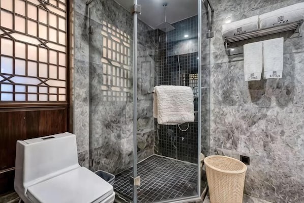 A bathroom with a glass shower enclosure, a white toilet, and a wicker basket.