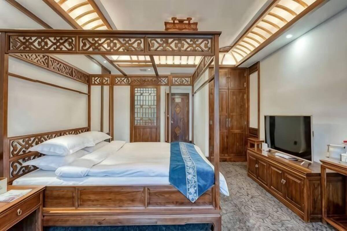 Un lit à baldaquin avec un téléviseur posé sur une commode en bois, un miroir et une armoire en bois.