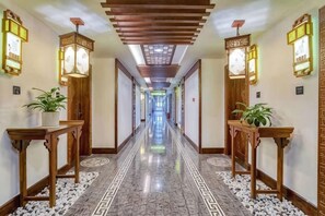 A hotel hallway with a reflective floor, wooden tables with potted plants, and wall-mounted light fixtures. - Taijiang Hotel (Taijiang)