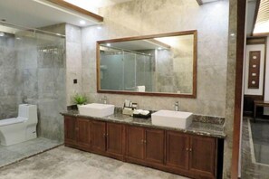 Un baño con tocador de mármol, dos lavamanos, un espejo grande y cabina de ducha.