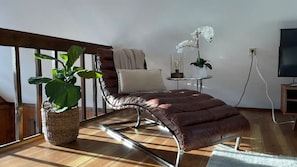 Un salon moderne avec un canapé en cuir, une grande plante en pot, une petite table sur laquelle est posée une orchidée blanche et un téléviseur sur un meuble en bois.