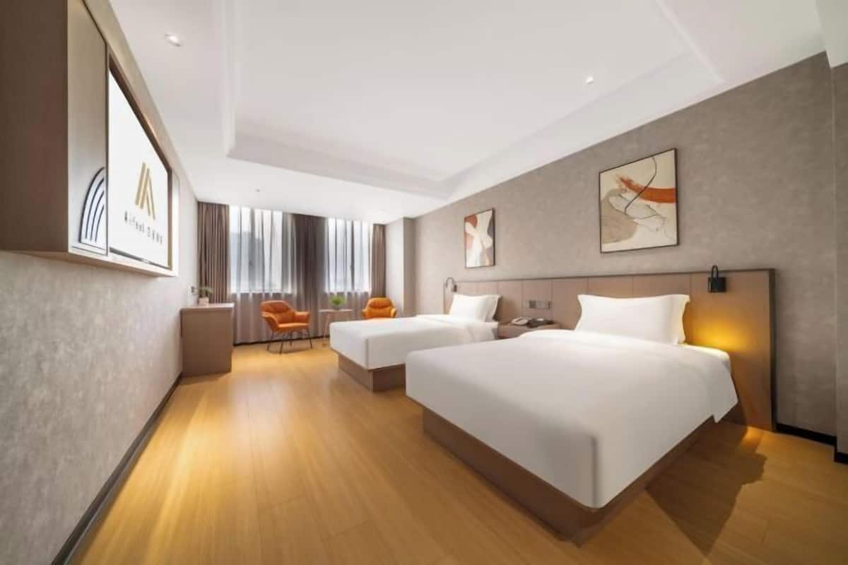 A modern hotel room with two beds, a seating area with chairs, and artwork on the walls.
