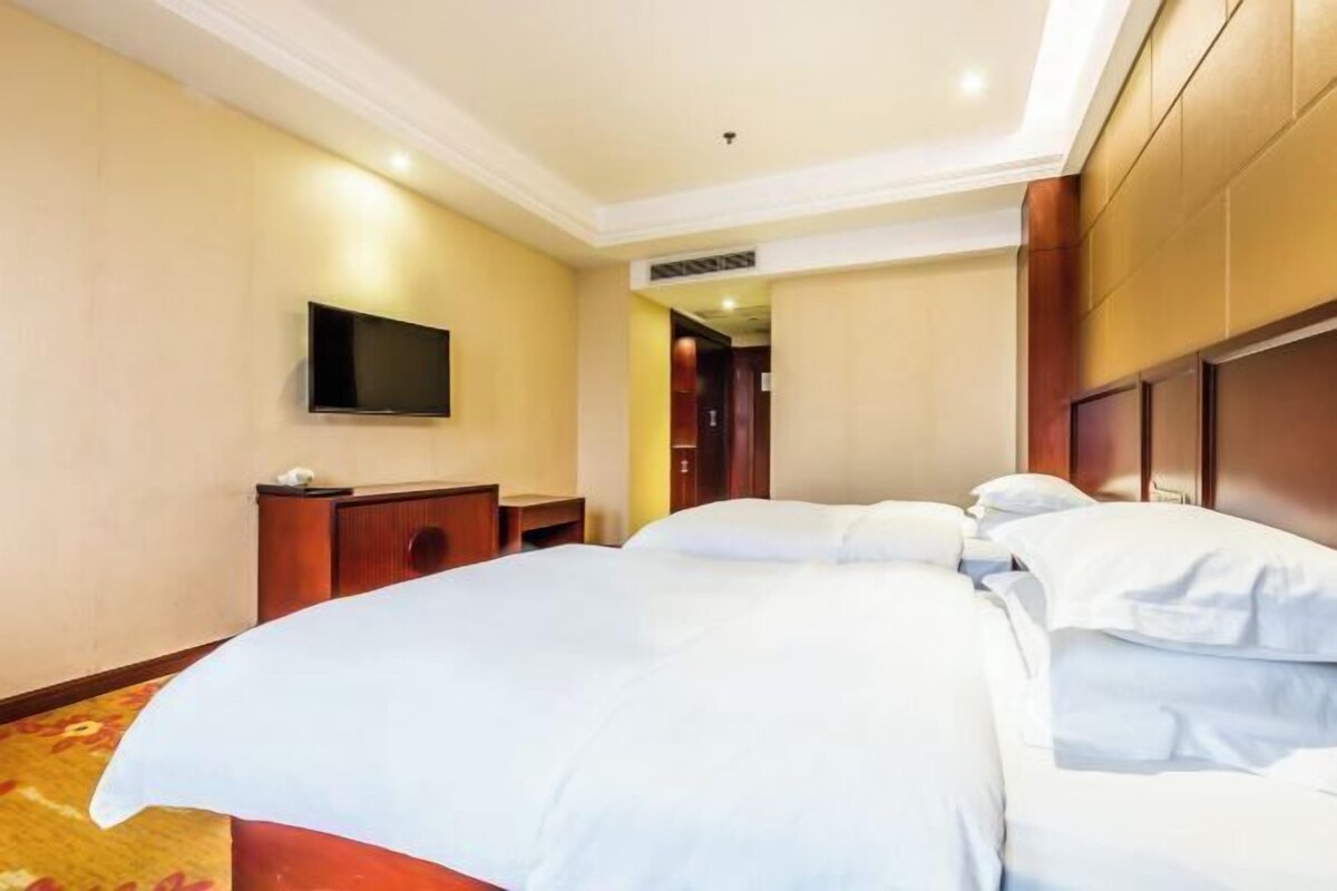 Ein Hotelzimmer mit einem großen Bett, einem flachbildfernseher an der Wand und einem hölzernen Kopfteil.