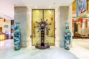 Eine Lobby mit dekorativer Wand, die ein Steuerrad, zwei große Vasen mit traditionellen Mustern und einen Empfangstresen im Hintergrund zeigt.