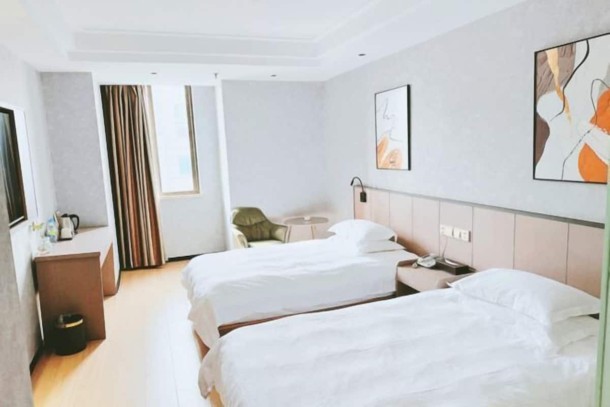 A hotel room with two beds, a small desk with a chair, a round table, and artwork on the walls.