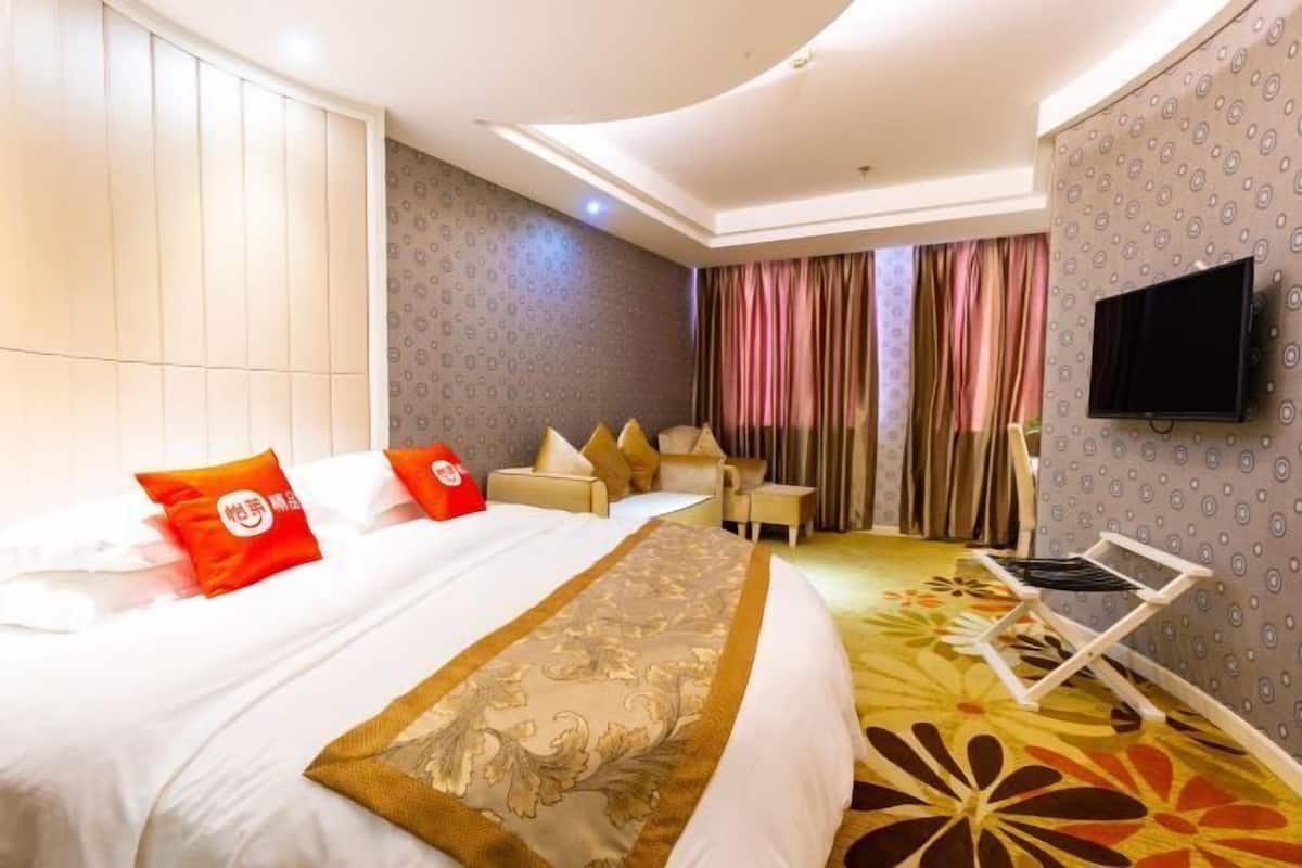 A hotel room with a large bed, a desk, a TV, and a patterned carpet.