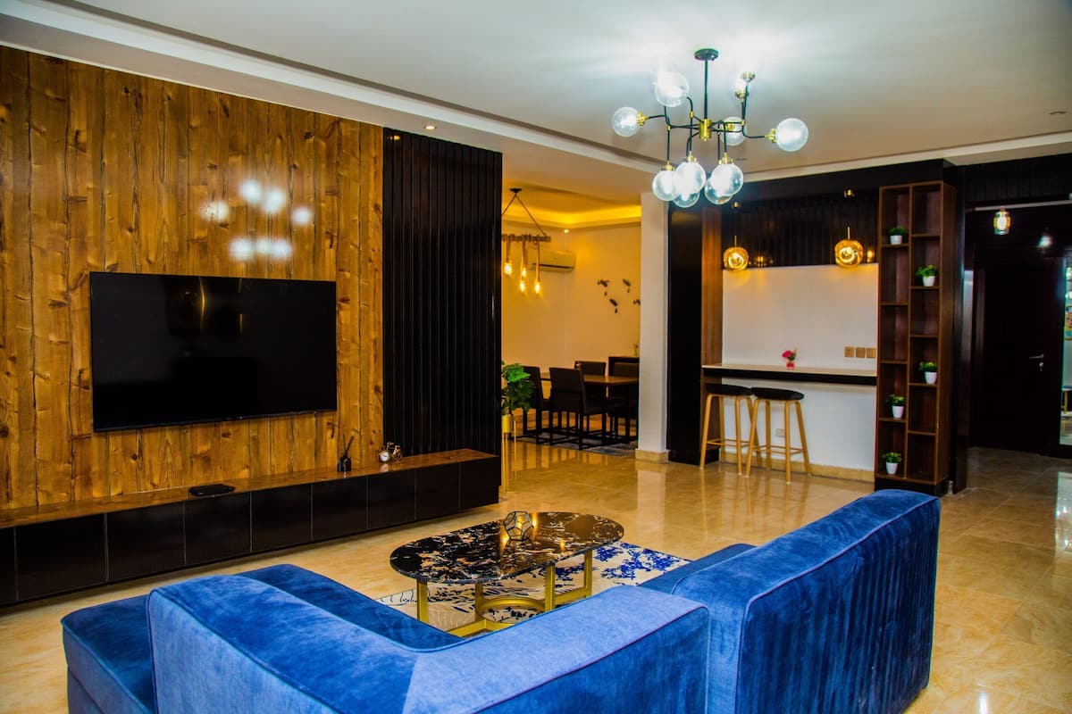 Una sala de estar moderna con televisor de pantalla plana, sofá azul, mesa de centro y una pared de acento de madera.