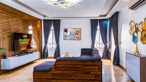 Un salon moderne avec un canapé d’angle en bois, un téléviseur à écran plat et un grand tableau abstrait accroché au mur.