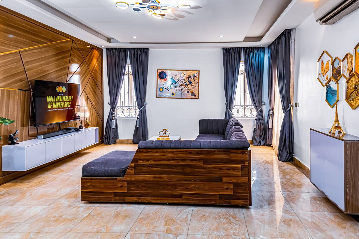 Una sala de estar moderna con un sofá seccional de madera, un televisor de pantalla plana y un cuadro abstracto grande en la pared.