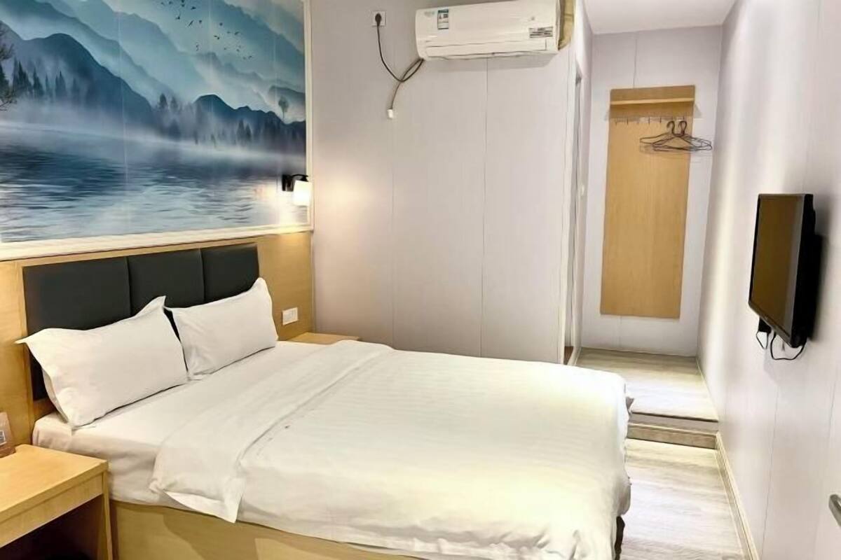 Et hotelværelse med en seng, en vægmonteret klimaanlæg, en trædør og et fjernsyn.