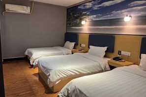 Une chambre d’hôtel avec trois lits simples, un climatiseur fixé au mur et un tableau représentant une scène de plage.