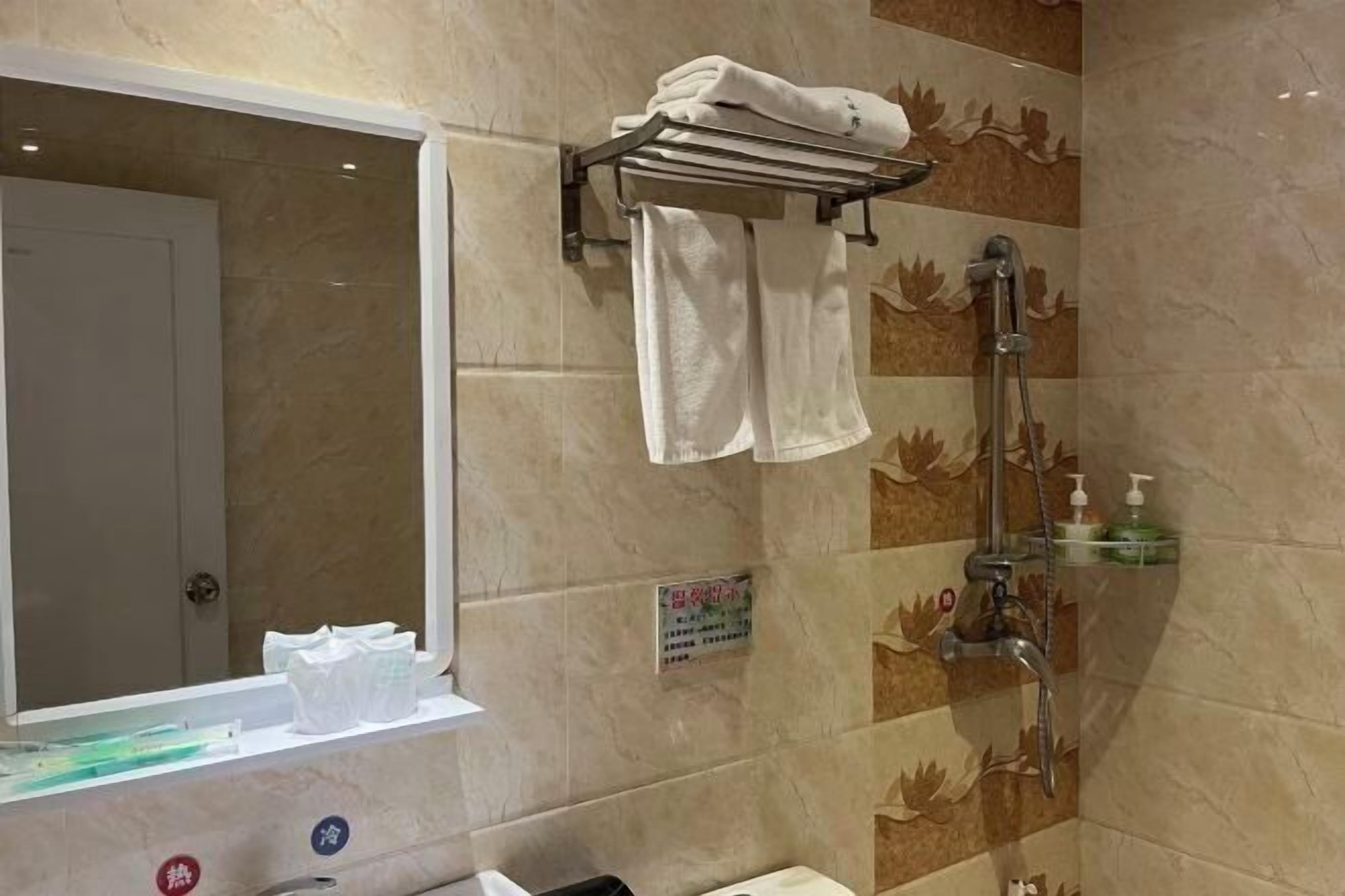 A bathroom with a shower, a towel rack, a mirror, and a shelf with toiletries.