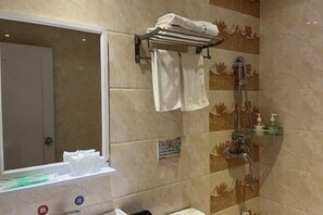 Une salle de bain équipée d’une douche, d’un porte-serviettes, d’un miroir et d’une étagère où sont rangés les articles de toilette.
