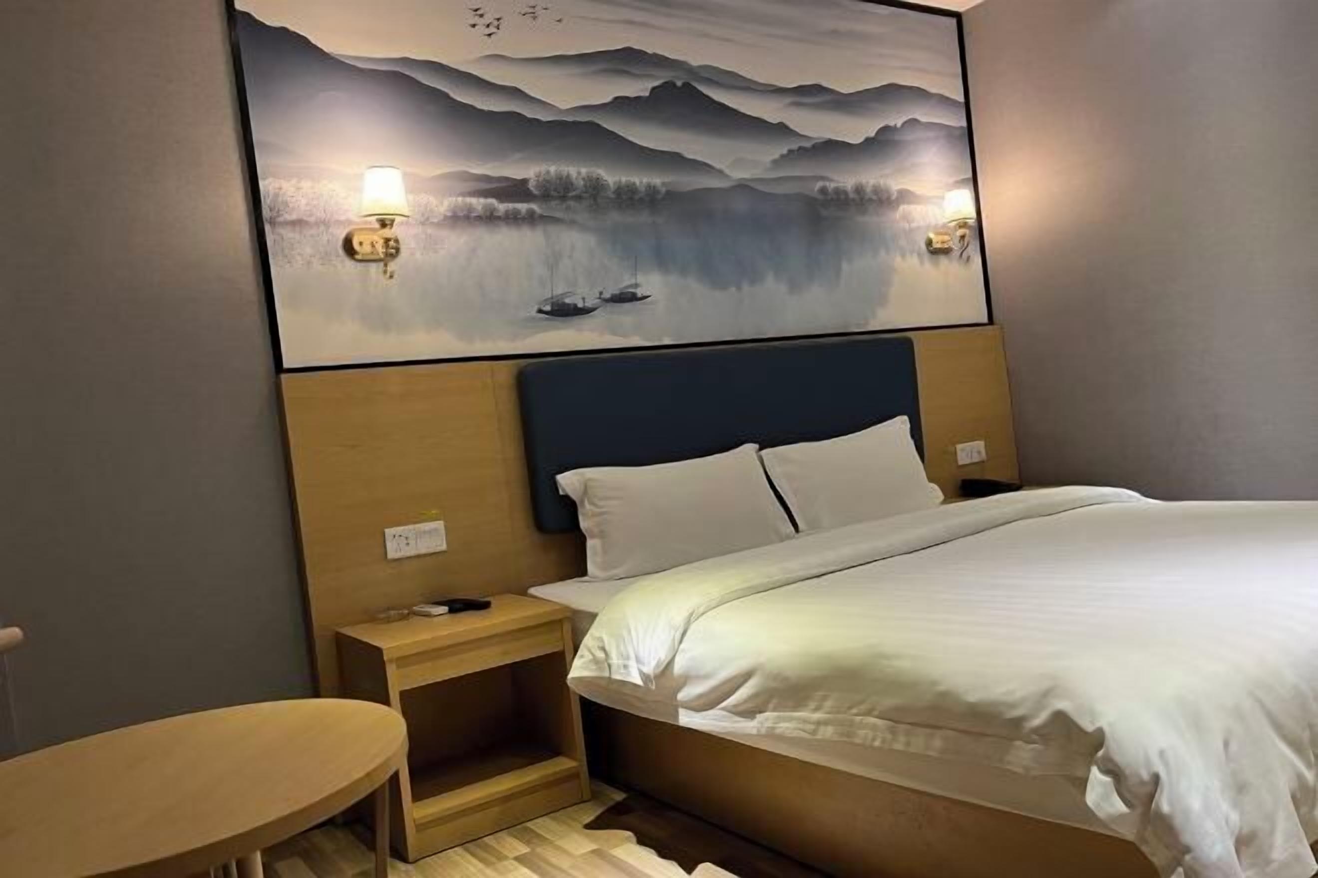 Une chambre d’hôtel avec un lit, des tables de chevet, un tableau accroché au mur et une petite table en bois.