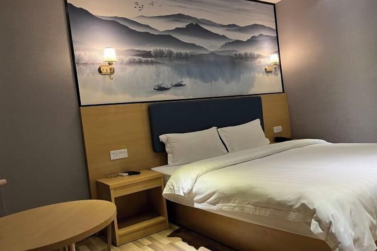 Une chambre d’hôtel avec un lit, des tables de chevet, un tableau accroché au mur et une petite table en bois.