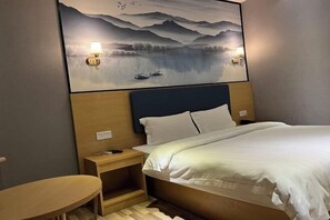 Une chambre d’hôtel avec un lit, des tables de chevet, un tableau accroché au mur et une petite table en bois.