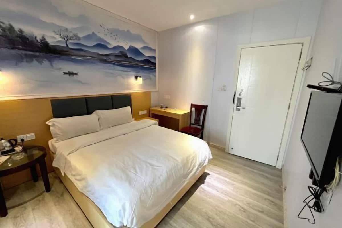 Et hotelværelse med seng, natbord, skrivebord, stol, fjernsyn og en dør.