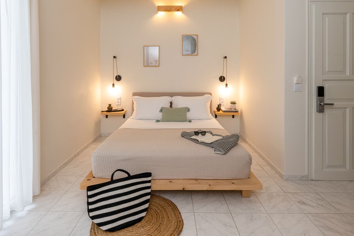 A bedroom with a bed, bedside tables, a hanging light fixture, a door, and a window with curtains.