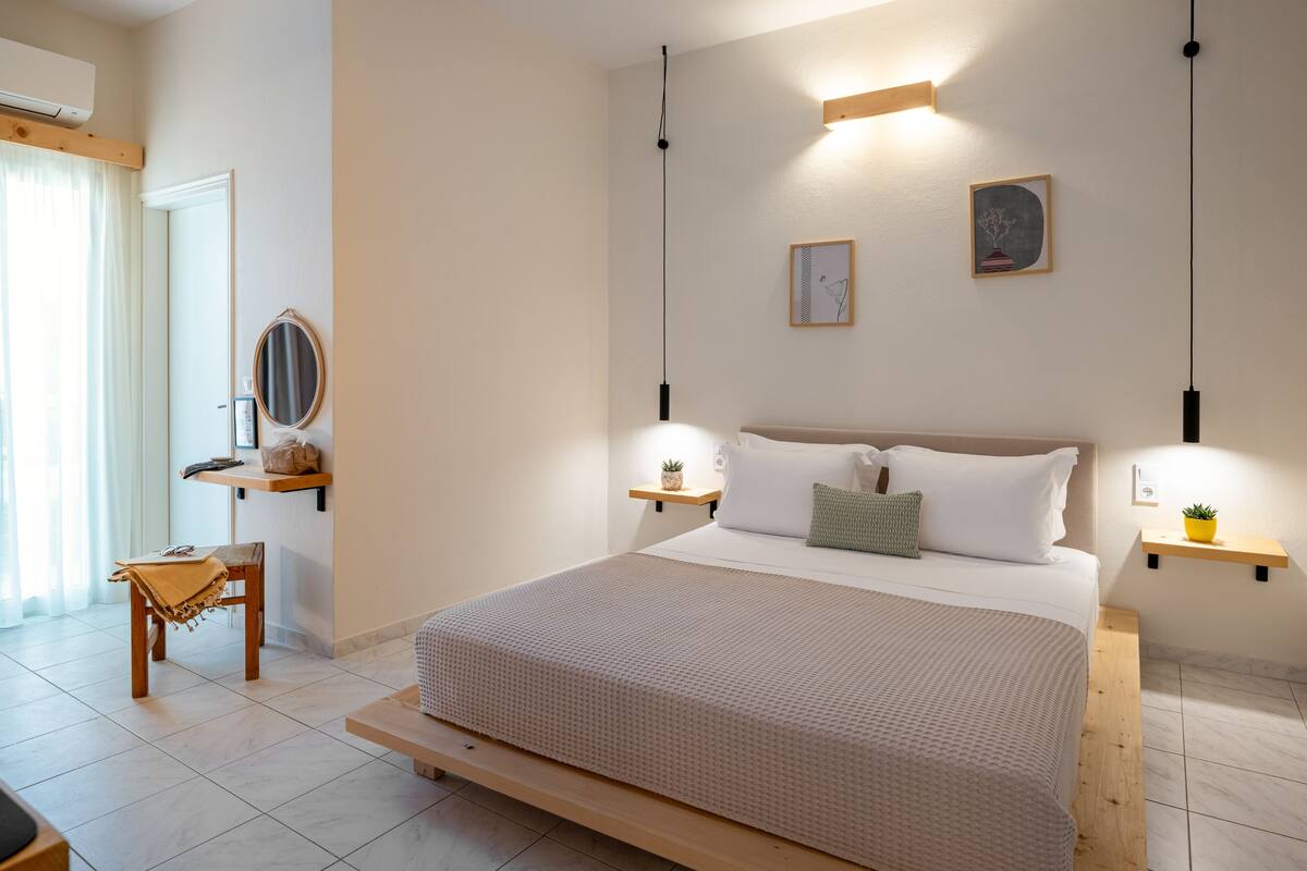 A well-lit bedroom with a large bed, bedside tables, a mirror, and artwork on the walls.