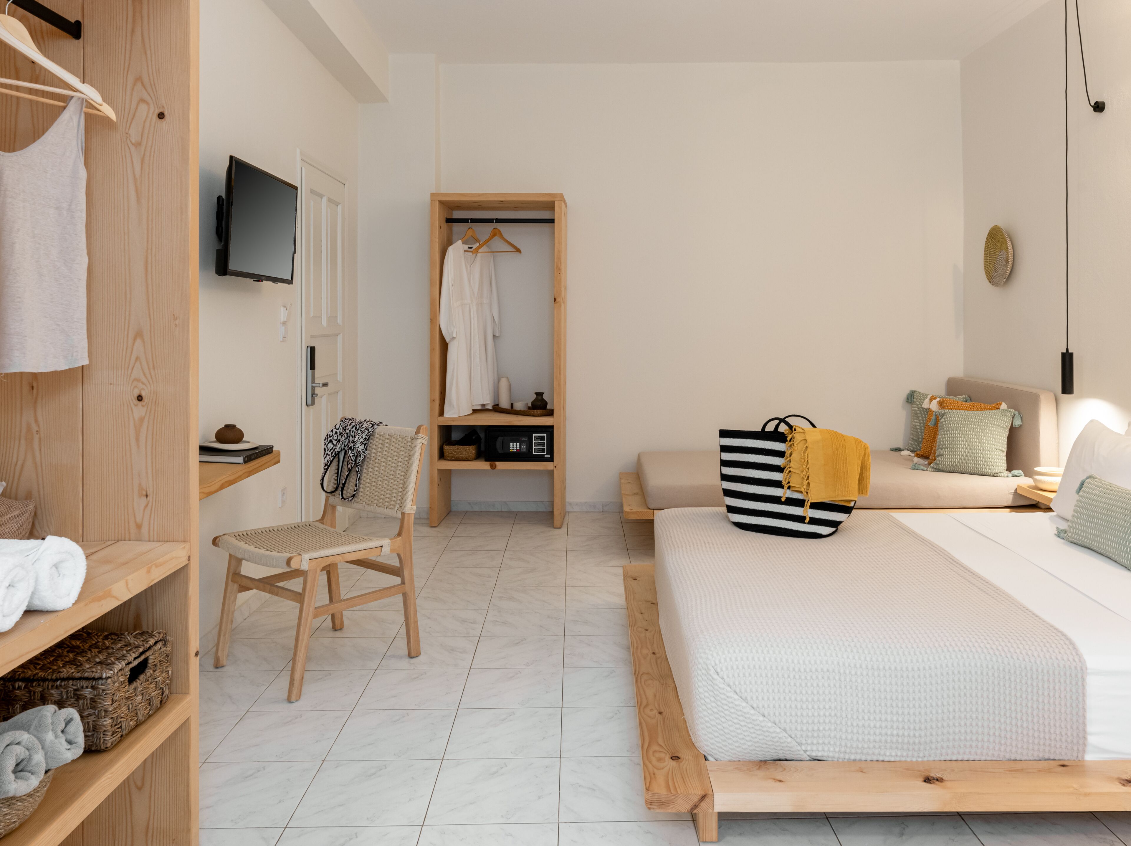 A bedroom with a bed, a chair, a wardrobe, a TV, and a shelf with towels.