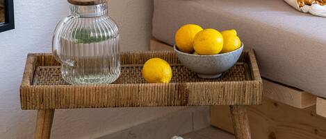 A wicker side table with a glass jar and a bowl of lemons, placed on a woven mat beside a sofa with a green and white patterned pillow.
