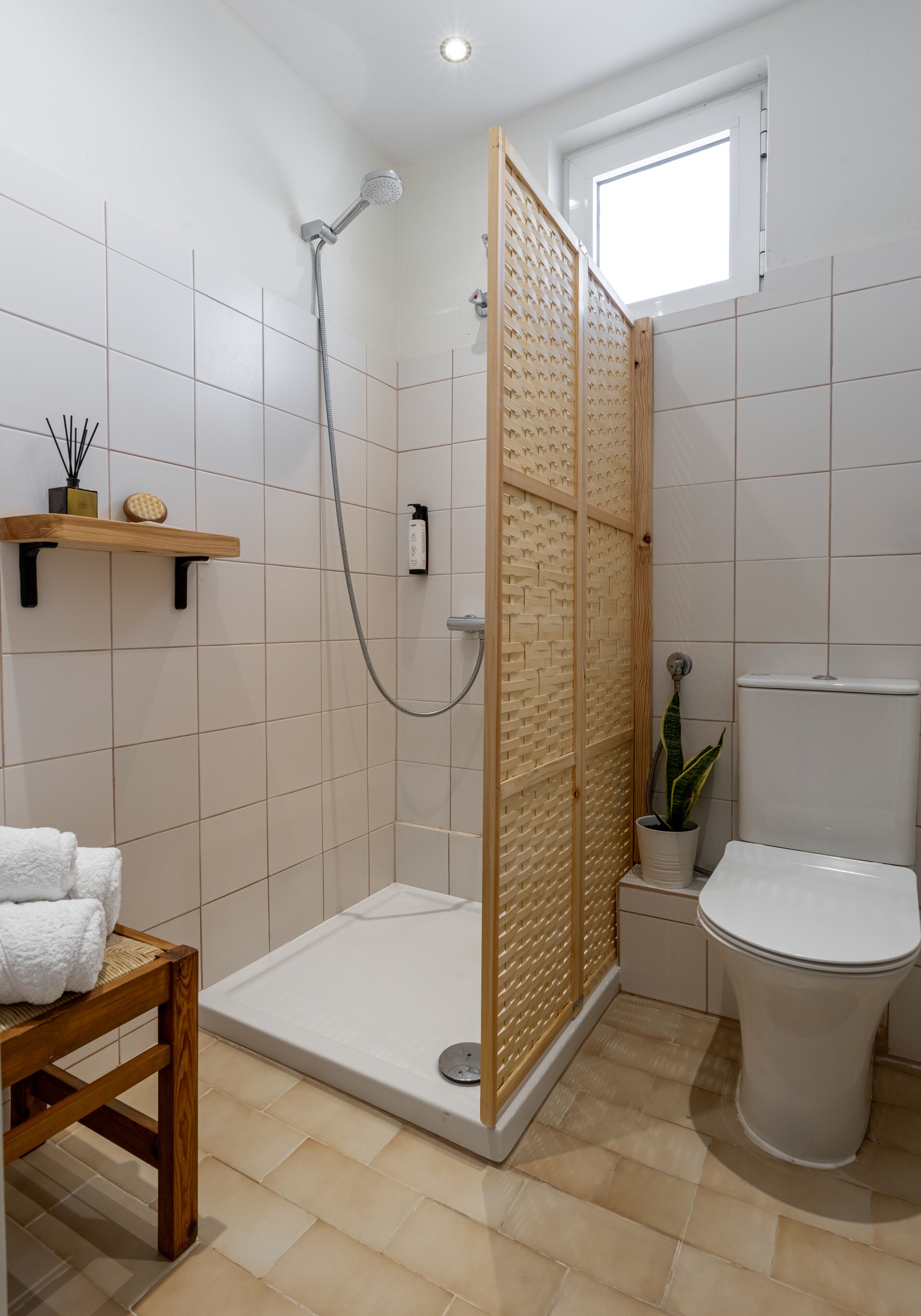 A modern bathroom with a shower, toilet, and a small seating area.