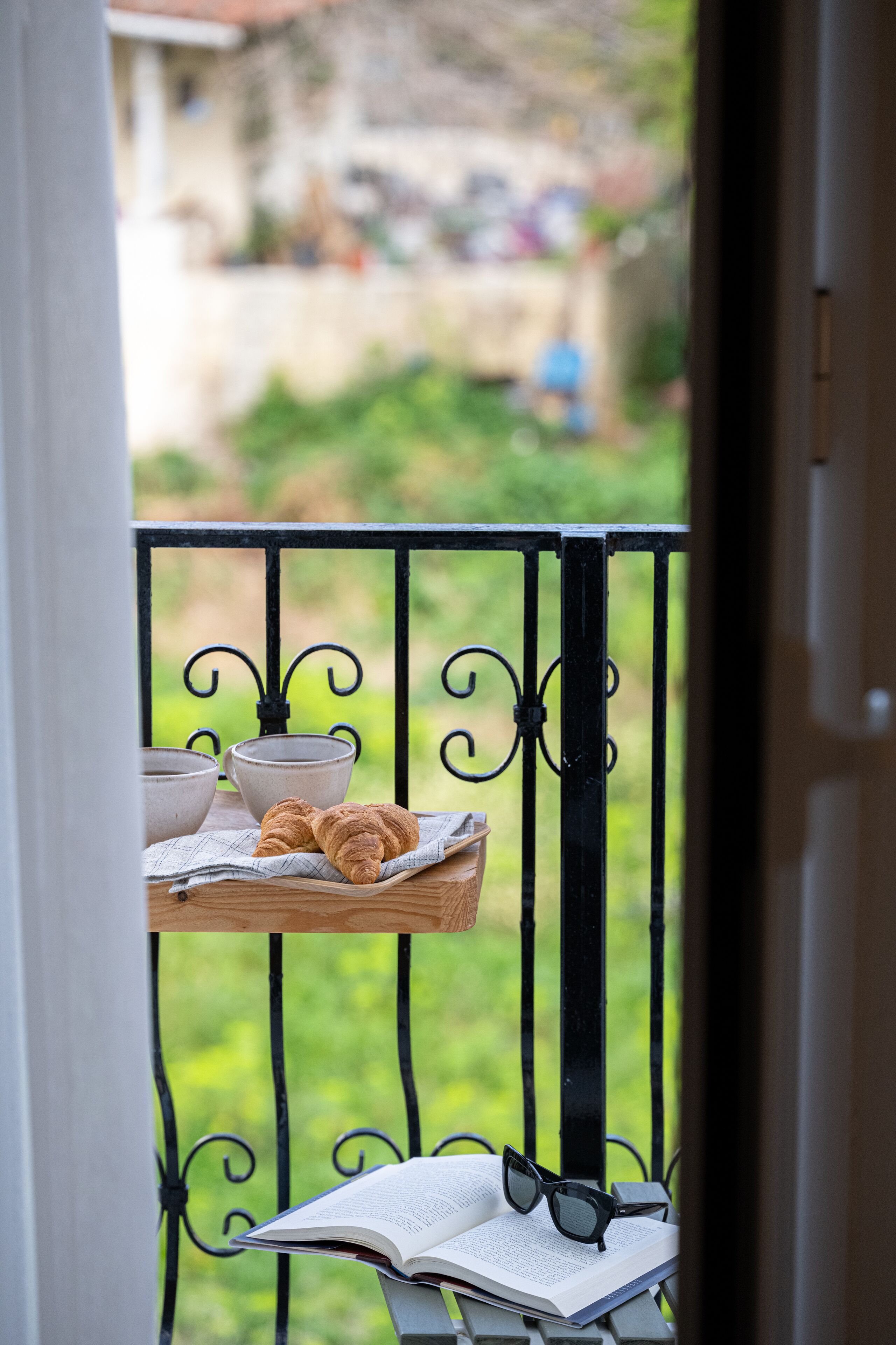 A balcony with a tray holding croissants, a bowl, and a book with glasses on it.