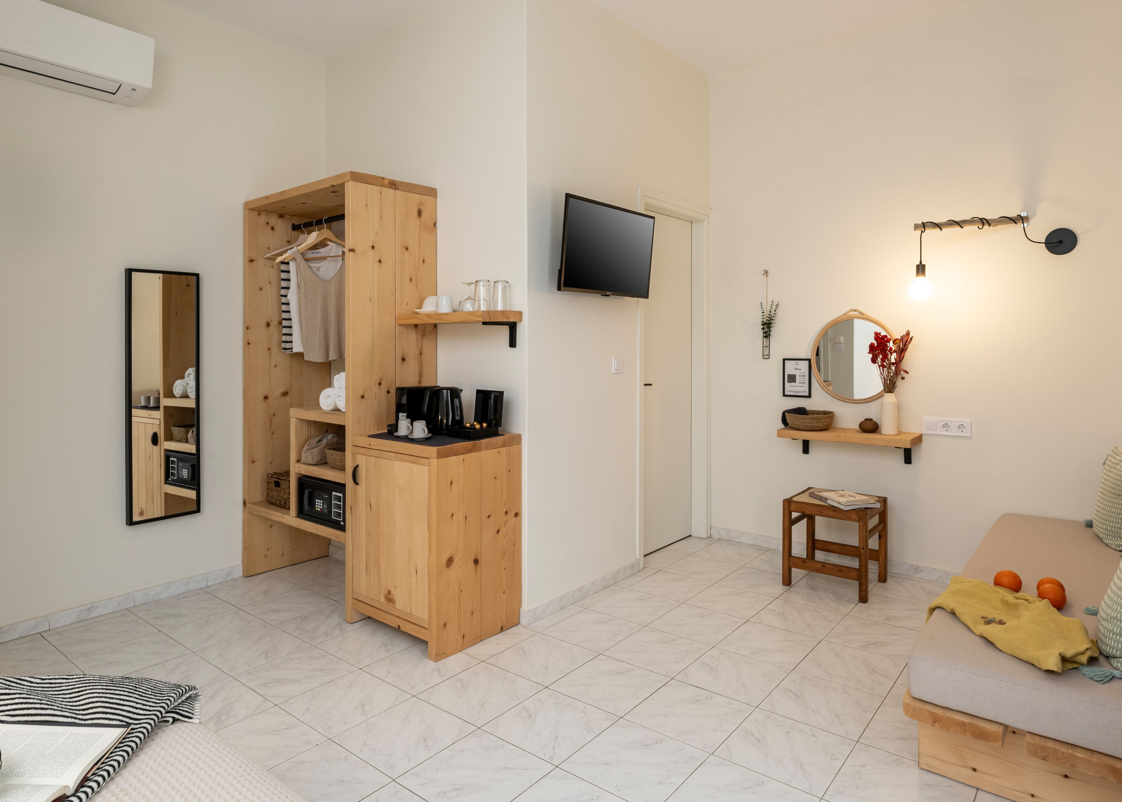 A neatly organized room with a wooden wardrobe, a television mounted on the wall, a small table with a chair, and a sofa.