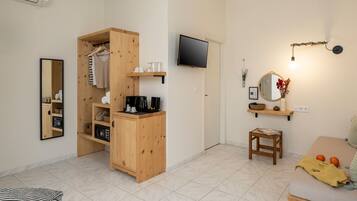 A neatly organized room with a wooden wardrobe, a television mounted on the wall, a small table with a chair, and a sofa.