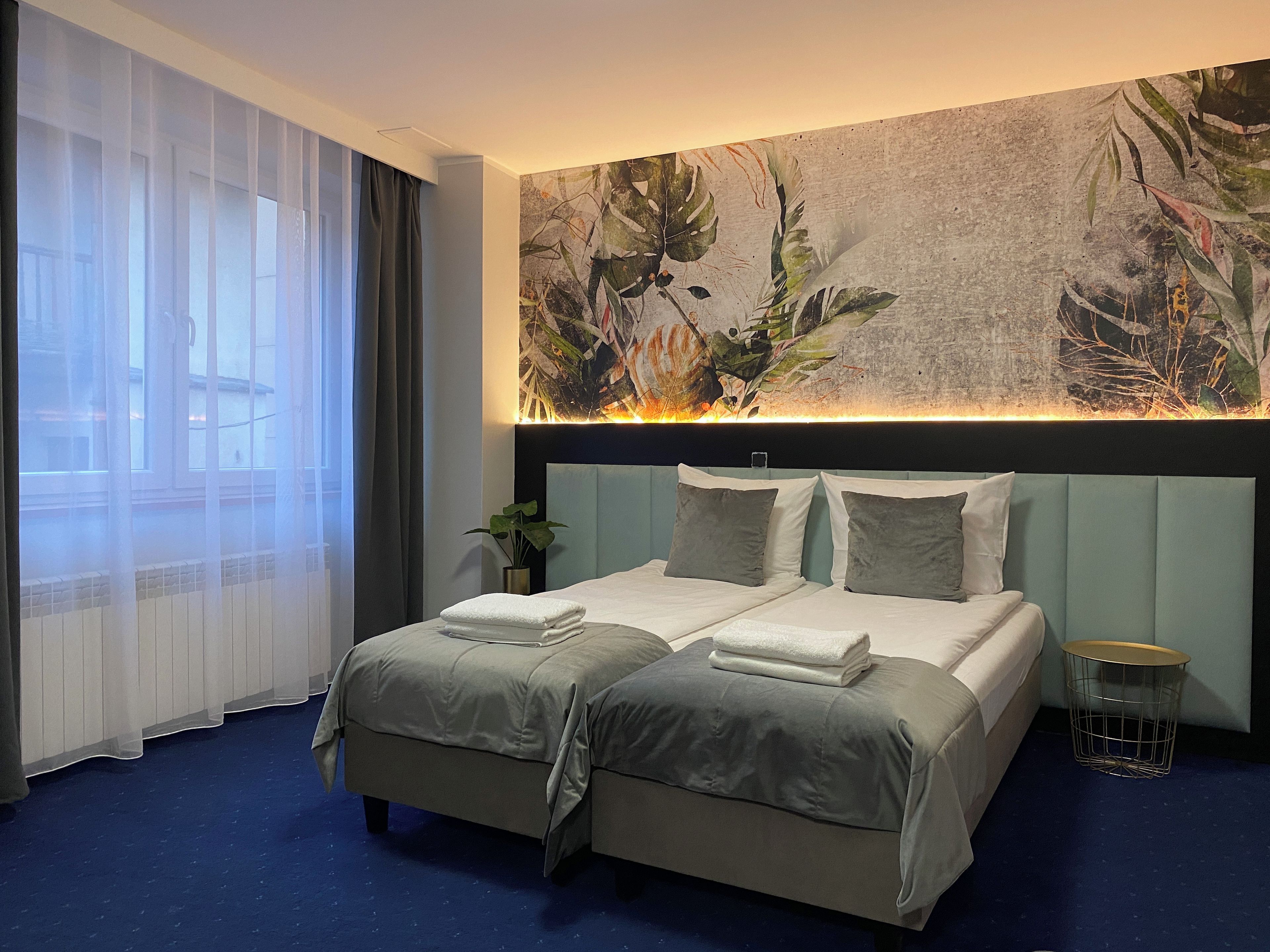 Ein Hotelzimmer mit Bett, Pflanze, Wandkunst und einem Fenster mit Vorhängen.