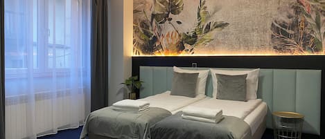 Una habitación de hotel con una cama, una planta, una obra de arte en la pared y una ventana con cortinas.