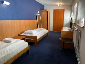 Une chambre d’hôtel avec deux lits simples, un bureau en bois, une chaise, un miroir, une télévision et un radiateur.