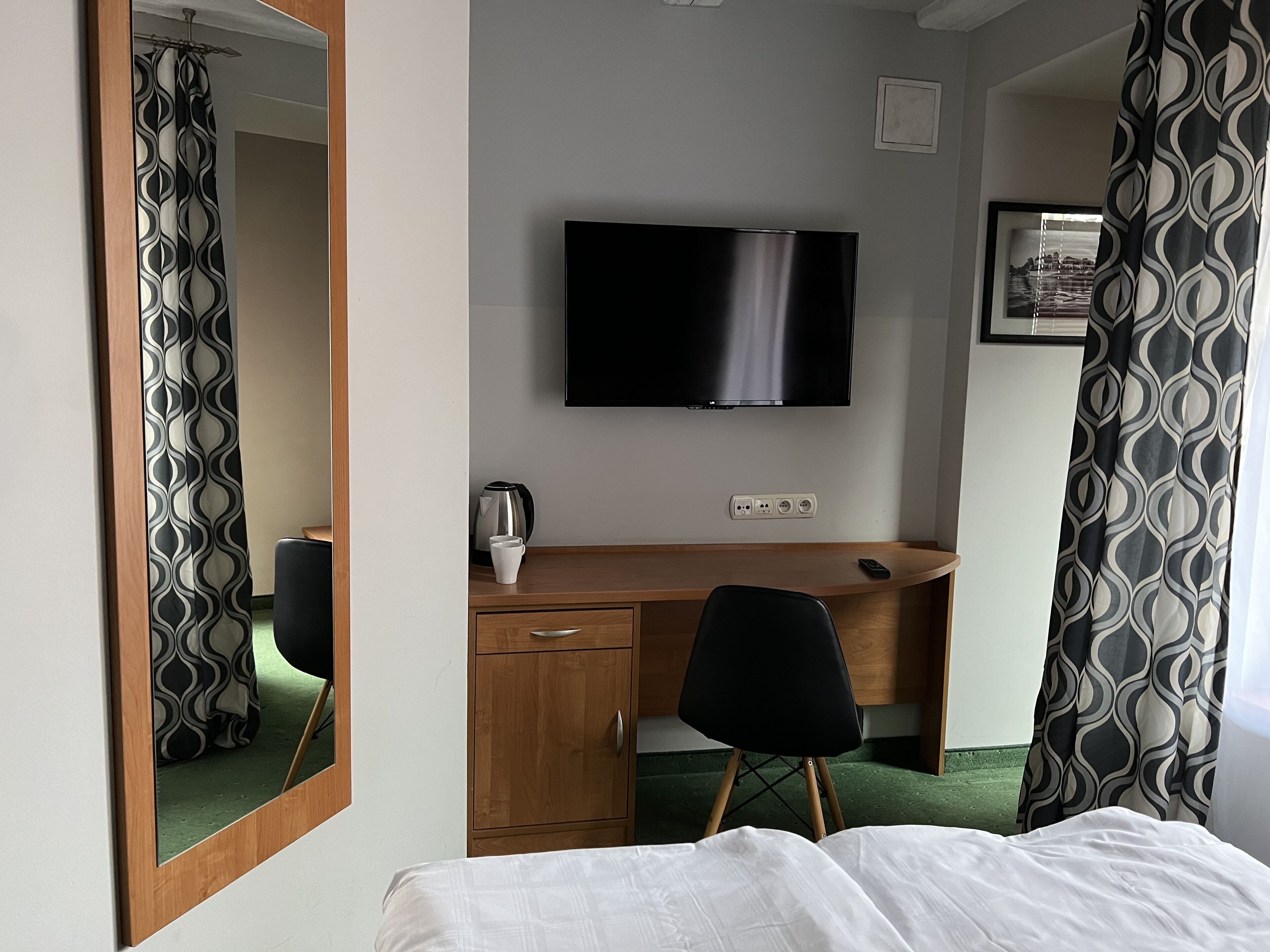 A hotel room with a bed, a desk with a television, a coffee maker, and a mirror.