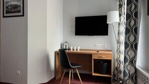Habitación de hotel con escritorio de madera, silla negra y televisor de pantalla plana montado en la pared.