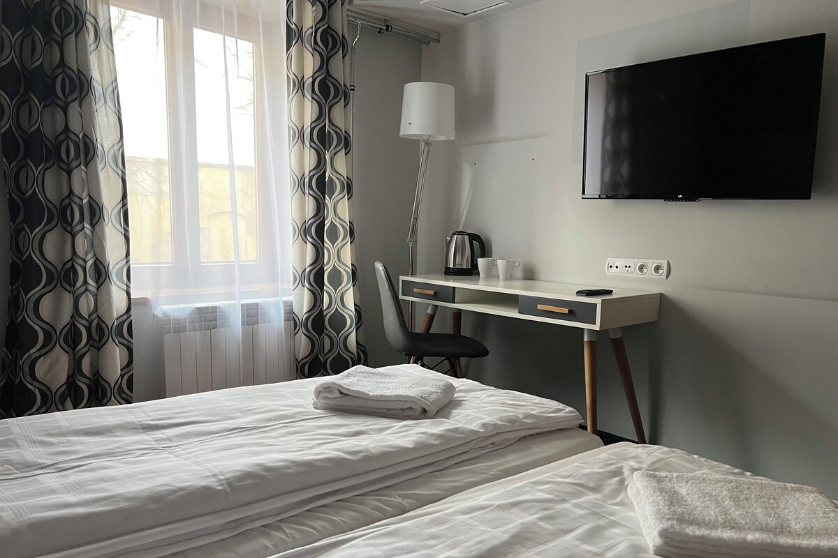 A hotel room with two beds, a desk with a chair, a TV, and a radiator.