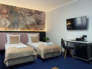Une chambre d’hôtel avec deux lits, un bureau, une chaise, une télévision et un grand tableau abstrait accroché au mur.