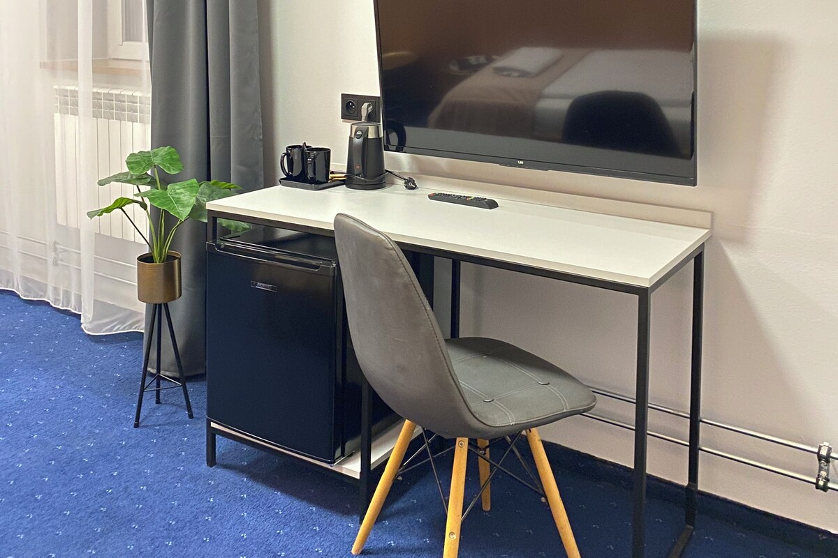 A compact workspace with a desk, chair, television, coffee maker, and a potted plant.