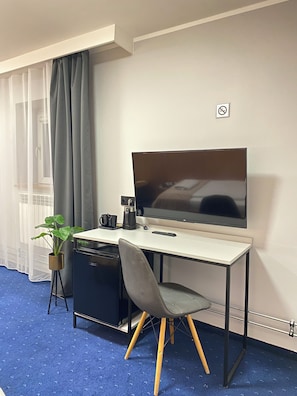 Une chambre d’hôtel de taille réduite, équipée d’un bureau, d’une chaise, d’une télévision et d’une petite plante en pot.